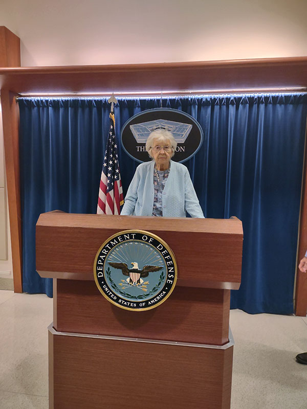 Mrs. Josephine Ann Talipin Gazelle posing behind a Pentagon podium with the DoD seal on it